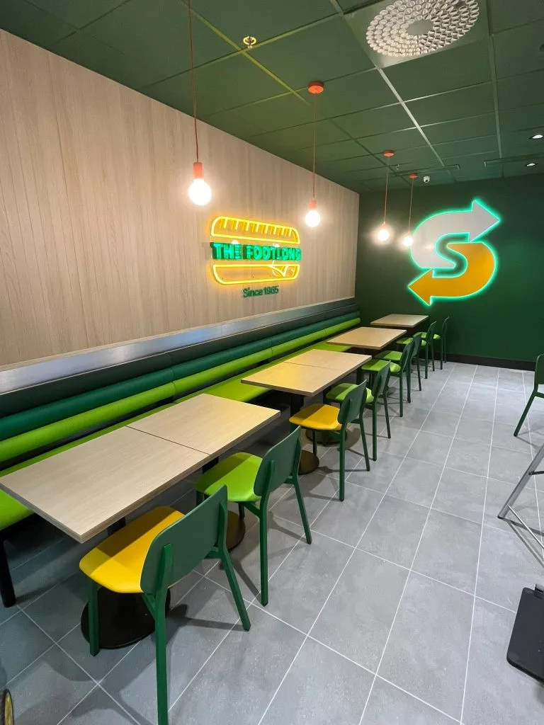 Subway-ravintolan asiakastila ja valaistu logoseinä